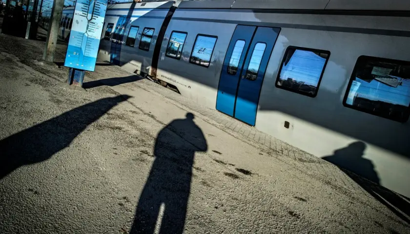 En skugga av en person står vid en tågvagn. En blå skylt med tåg linjer Stockholm syns bredvid.
