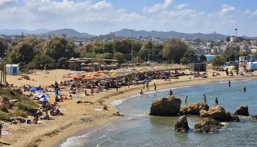 En livlig strand i Grekland med solbadare, parasoller och klippor. En perfekt hotellskatt för en solig semester.