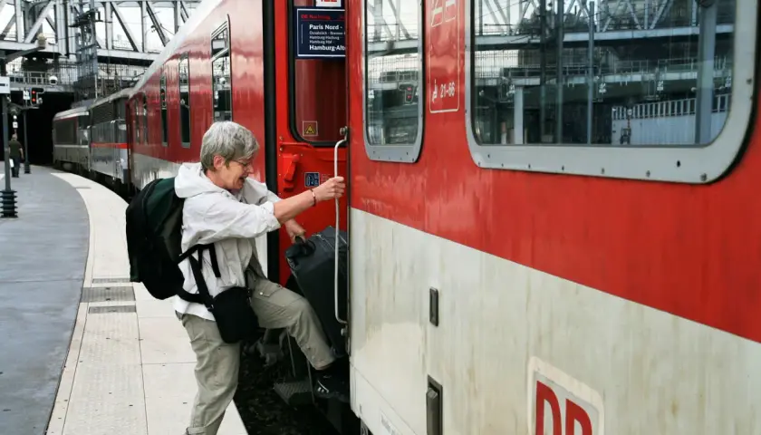 Äldre kvinna med ryggsäck och resväska kliver på ett rött tåg. Kanske början på en resa med interrailkort i Sverige.