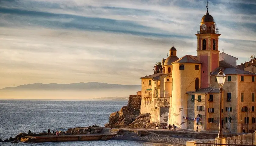 Solnedgång över Camogli, Italien. Kyrkan med sitt klocktorn lyser i kvällssolen vid havet.