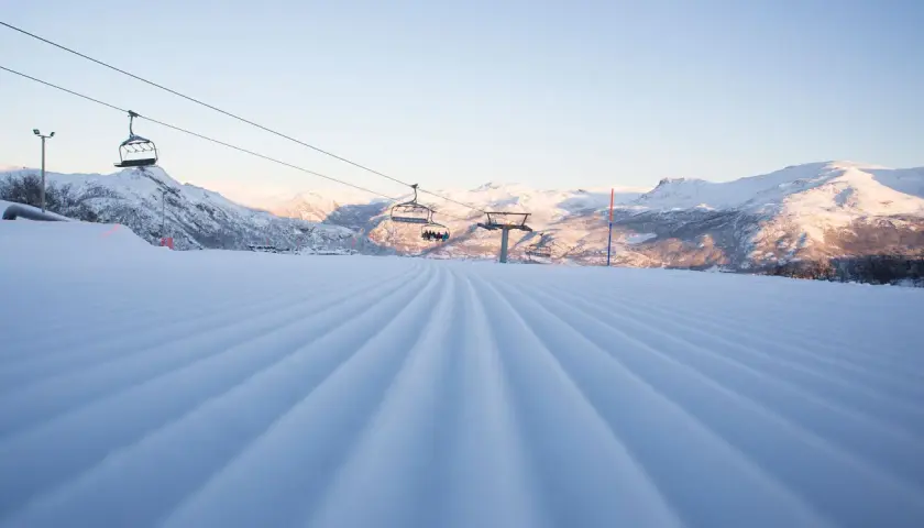 Perfekt pistad backe med sittliftar som tar skidåkare upp mot Hemsedal. Solen lyser på de snöklädda bergen.