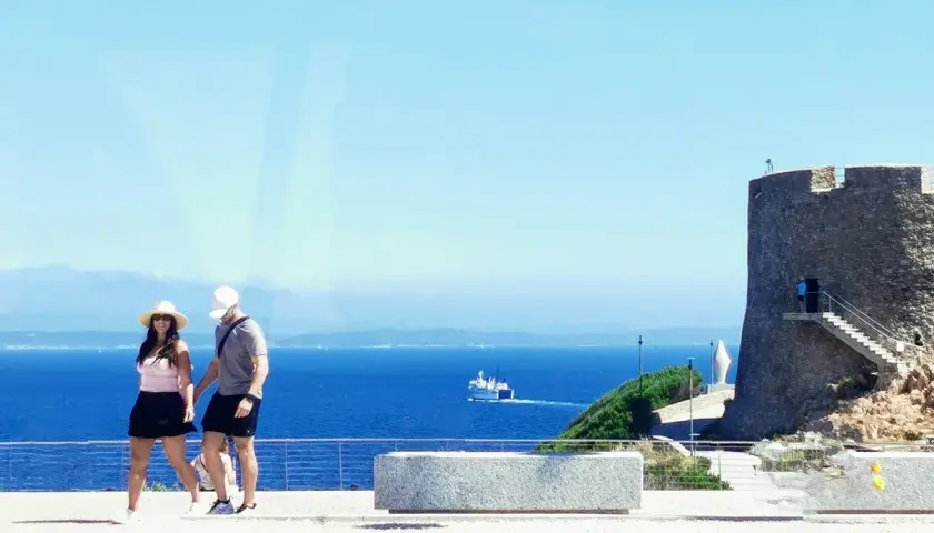 Ett par promenerar vid havet nära ett gammalt torn i Cagliari, Italien.