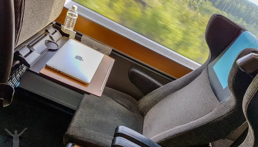 Bekväm sittplats i sj sovvagn 1 klass med laptop och vattenflaska. Landskapet susar förbi utanför fönstret.