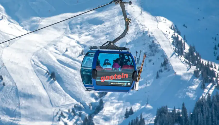 En blå gondol med skidåkare på väg uppför ett snöigt berg. Snart dags för tåg till St. Anton!