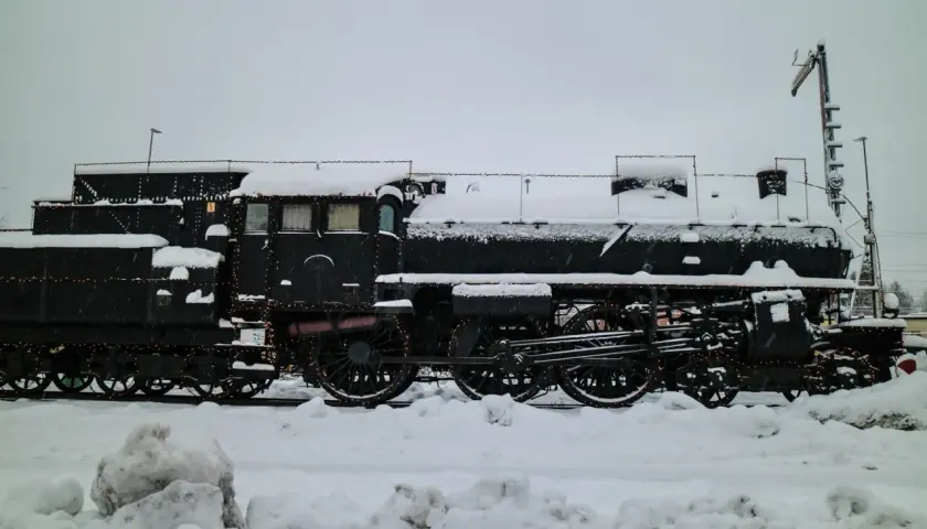 Ett snötäckt ånglok, dekorerat med ljusslingor, står parkerat. Kanske en del av ett biltåg i Tyskland som väntar på våren.