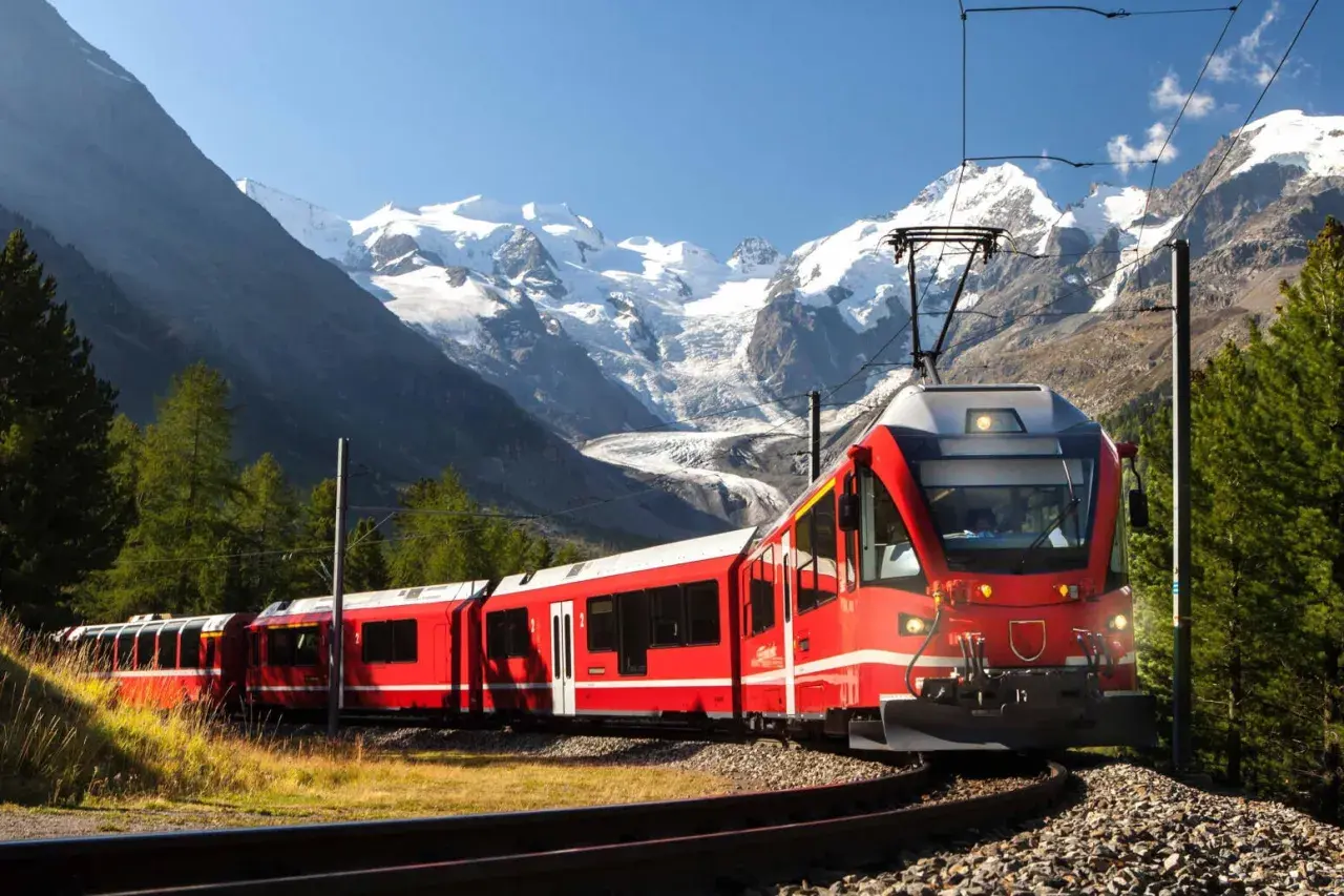 Ett rött tåg slingrar sig genom ett berglandskap med snöklädda toppar. Snart är det dags för nattåg till Italien.