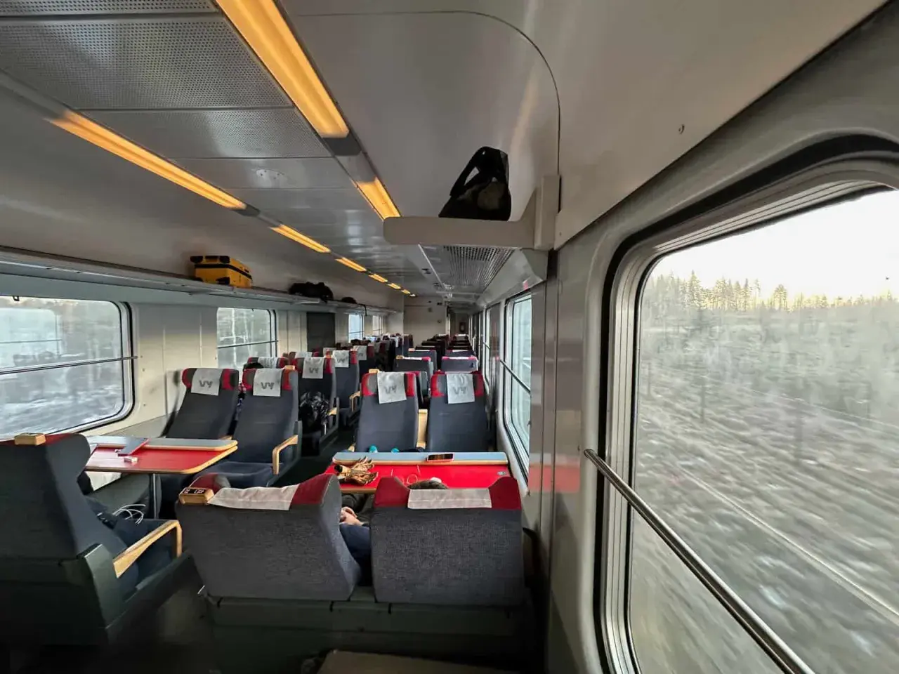 Vy-tåget mot Luleå från Stockholm. Tomma säten med röda bord och fönster med utsikt över snöig skog.