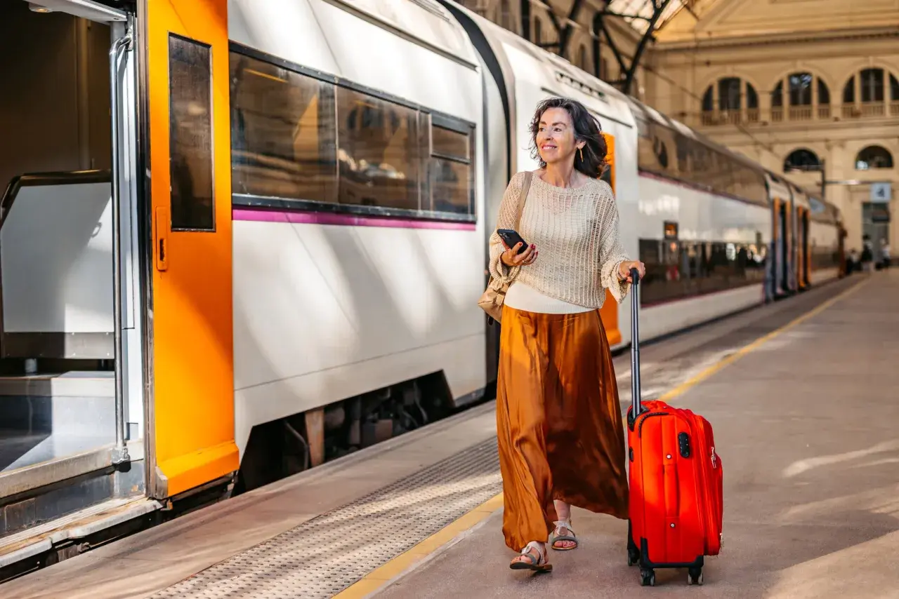 Kvinna med röd resväska och mobiltelefon på tågstationen, redo för sitt tågluffa Europa karta-äventyr.