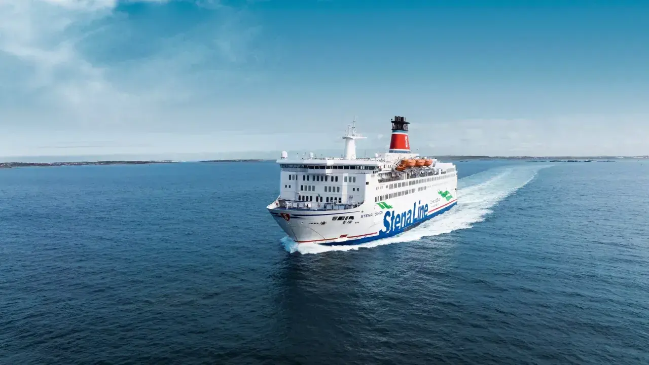 Stena Line-färja på väg till Danmark, med en stor vit skrov och blå linjer, lämnar ett vitt spår i det blå havet under en klarblå himmel.