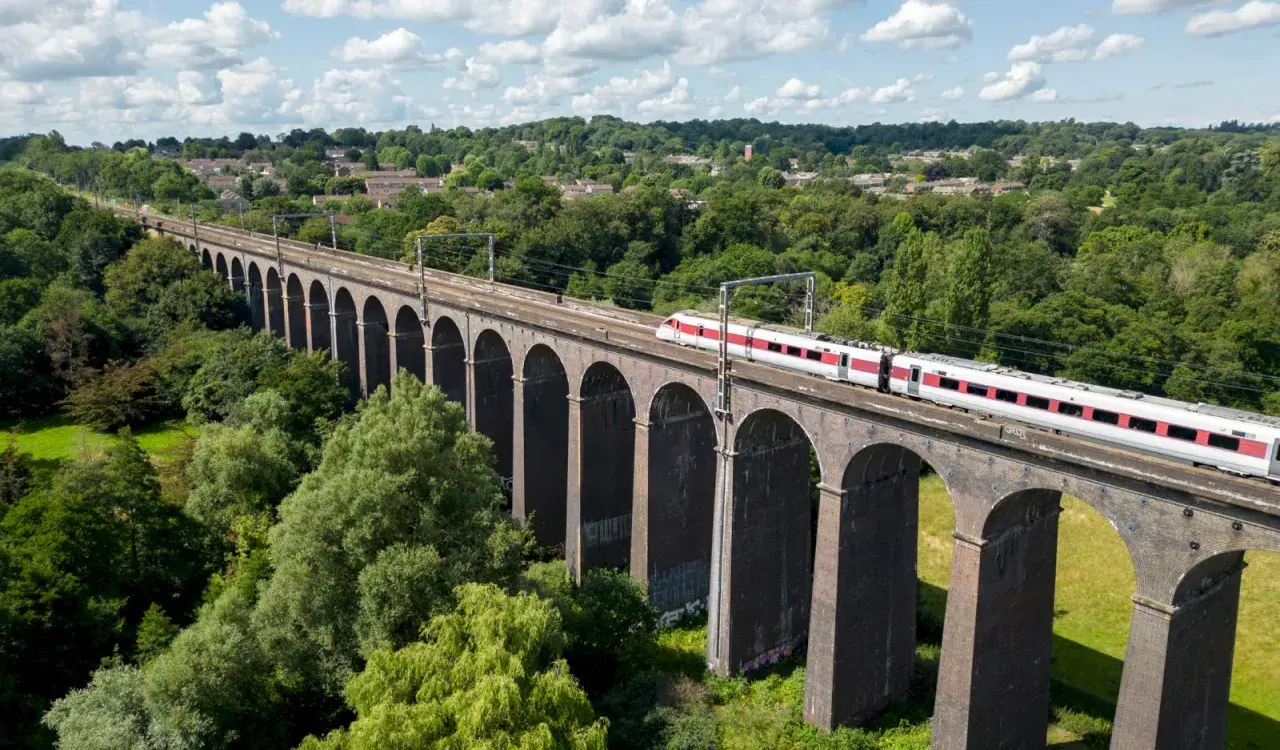 Ett modernt tåg susar fram över en gammal tegelbro, en perfekt bild för att tågluffa i England.