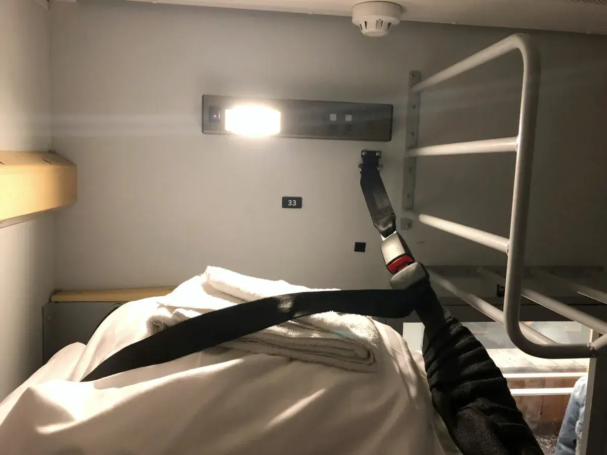 En bädd i en couchette train med vita lakan, handdukar och ett säkerhetsbälte.