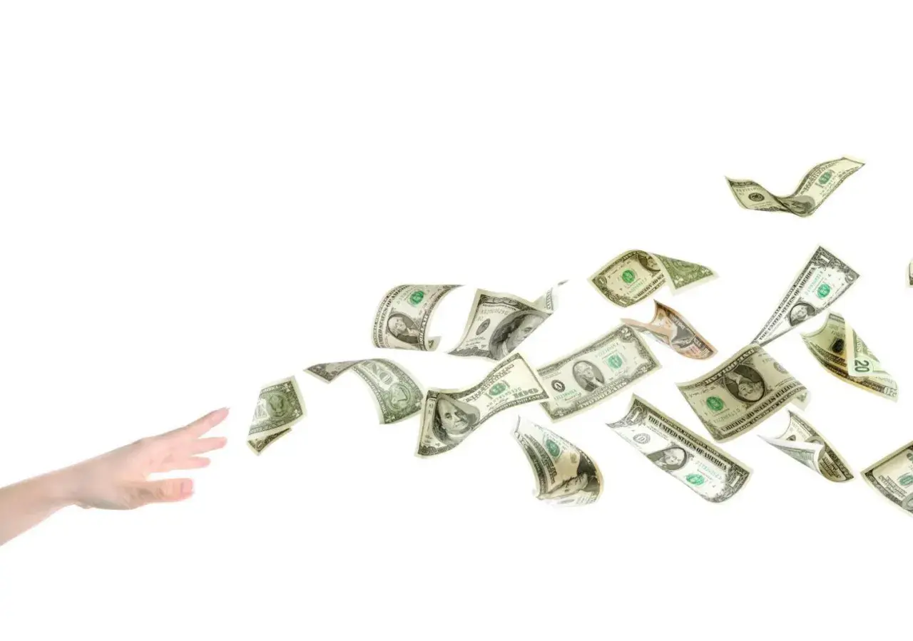 En hand sträcker sig efter flygande dollarsedlar, som om de vore en del av ett äventyr med tågluffarkort Europa.