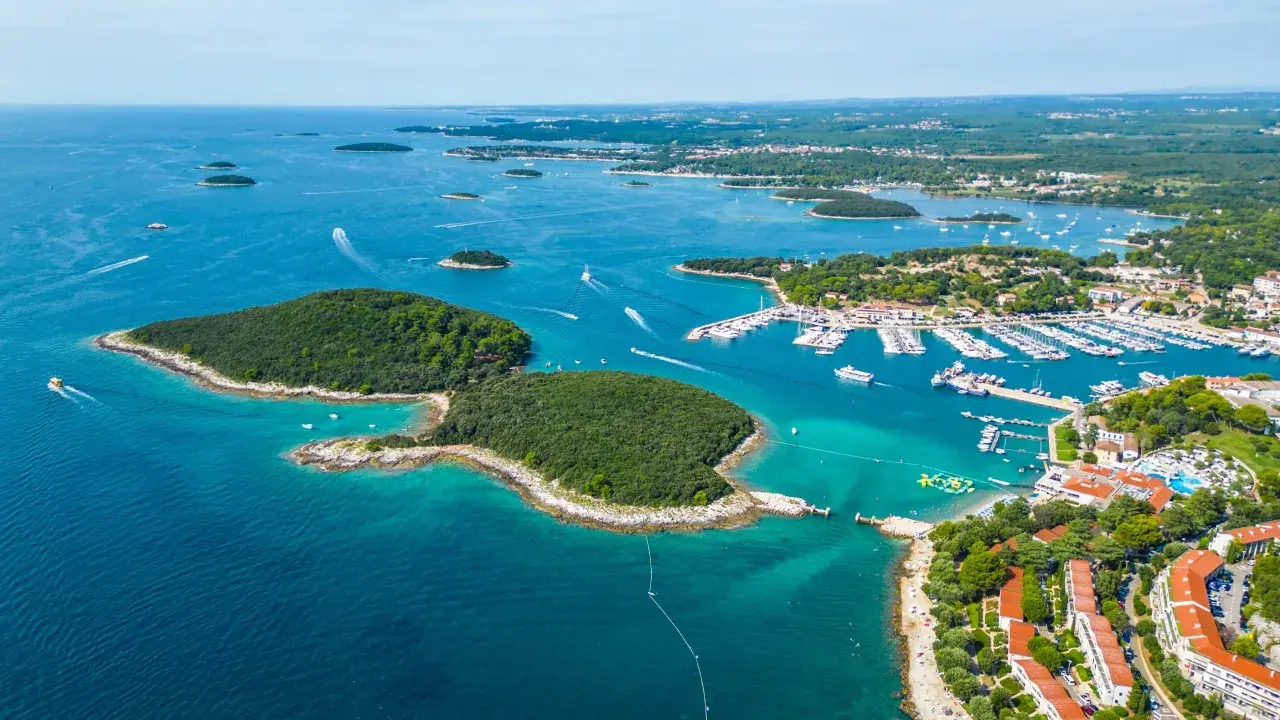 En vacker kustlinje i Kroatien med en stor marina full av båtar. En grönskande ö sticker ut i det turkosa vattnet.