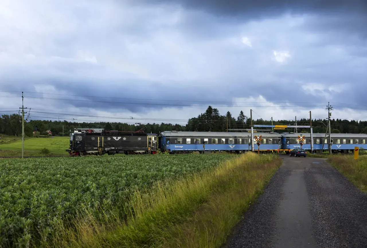 Ett svart lok drar blå sovvagnar på nya nattåg genom ett lantligt landskap med gröna fält och skog.