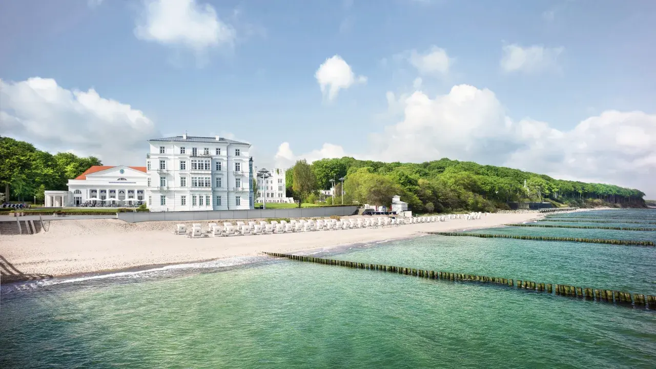 Vacker strand med vita strandstolar och hotell vid den tyska rivieran. Gröna träd och en blå himmel med moln.