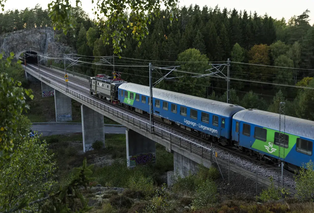 Ett blått SJ-tåg, kanske ett nattåg Berlin, korsar en bro genom en skogig miljö.