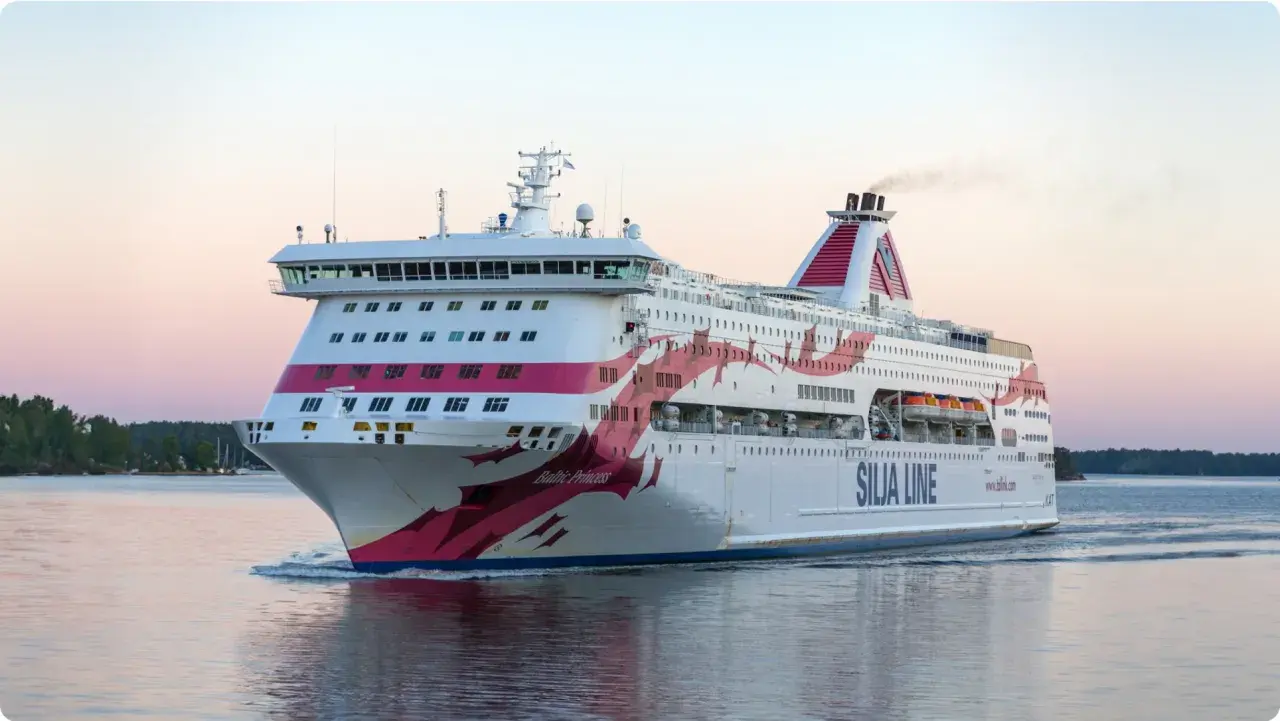 Silja Line-färja på en kryssning Stockholm-Åbo. En stor vit passagerarfärja med rosa dekorationer glider fram på vattnet i solnedgången.