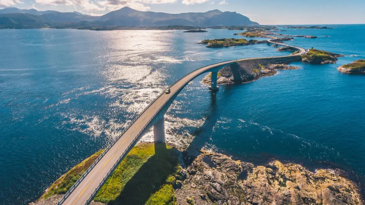 En bil kör på en bro över det glittrande havet i Norge. En dröm för alla som älskar att bila i Norge.