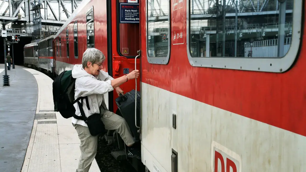 Äldre kvinna med ryggsäck och resväska kliver på ett rött tåg. Kanske början på en resa med interrailkort i Sverige.