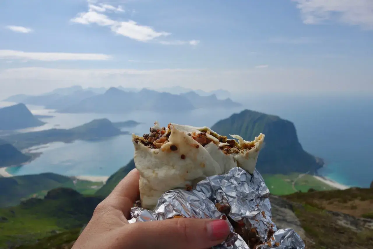 En hand håller en burrito med en fantastisk utsikt över Lofoten. En perfekt paus under vandringen.