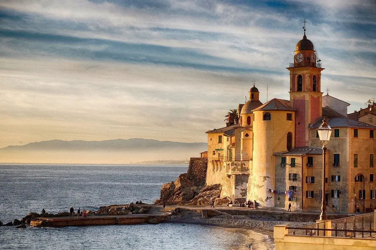 Solnedgång över Camogli, Italien. Kyrkan med sitt klocktorn lyser i kvällssolen vid havet.