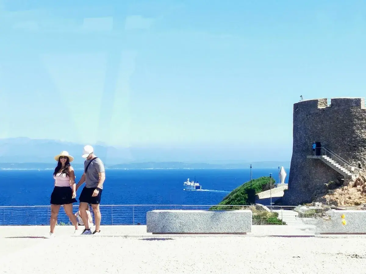 Ett par promenerar vid havet nära ett gammalt torn i Cagliari, Italien.