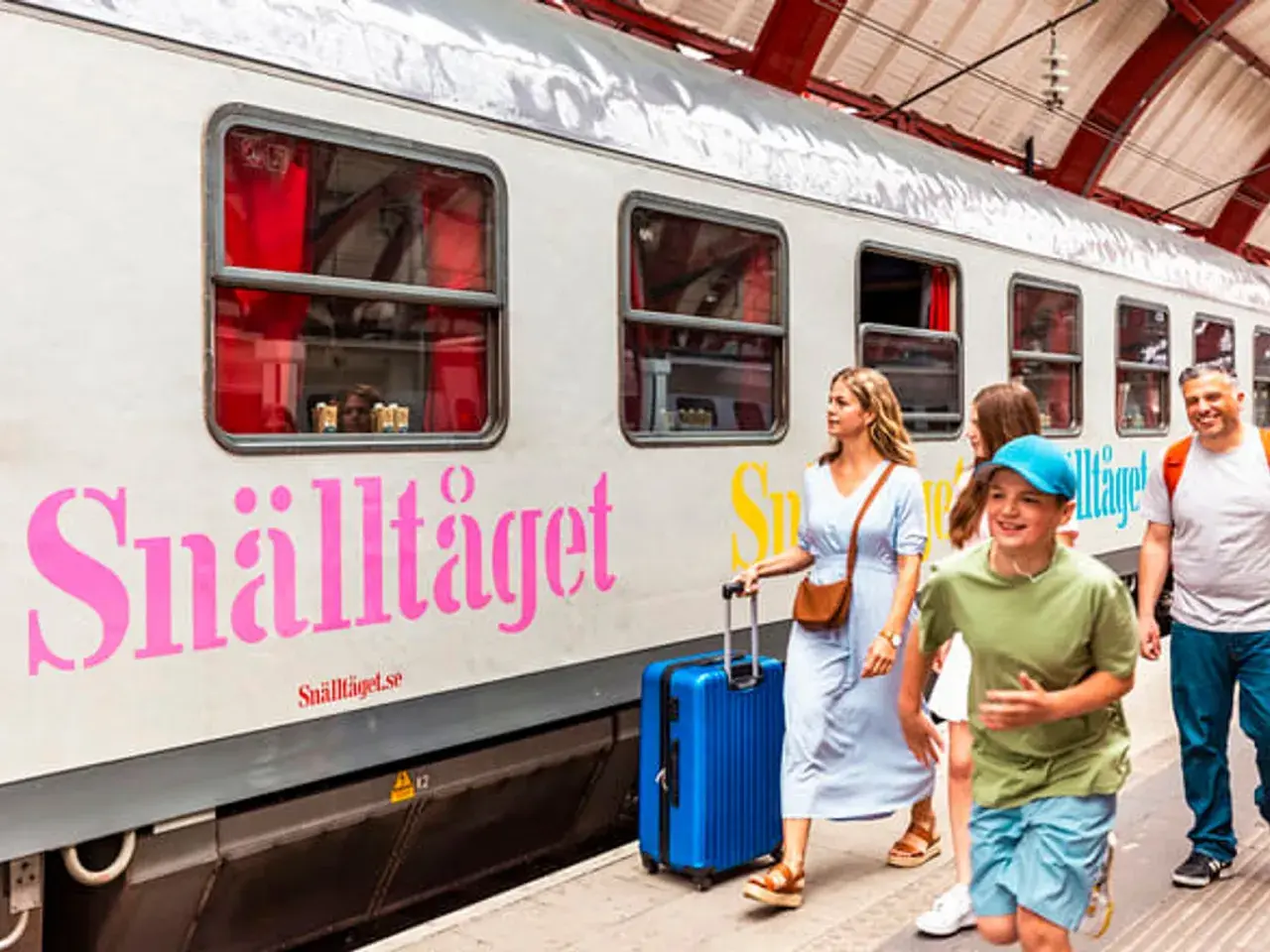 Familj på väg mot Stockholm med Snälltåget. Glada barn och vuxna med resväskor vid tåget.