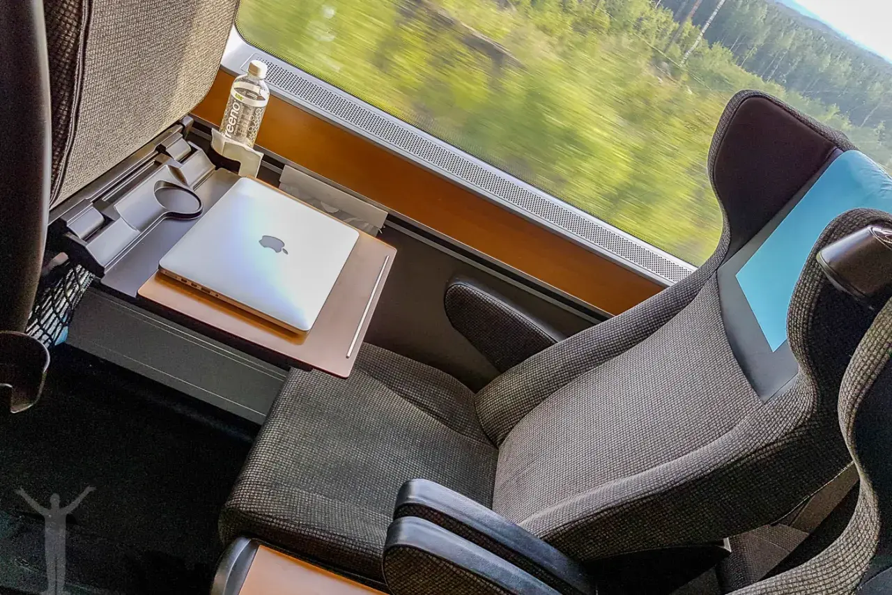 Bekväm sittplats i sj sovvagn 1 klass med laptop och vattenflaska. Landskapet susar förbi utanför fönstret.