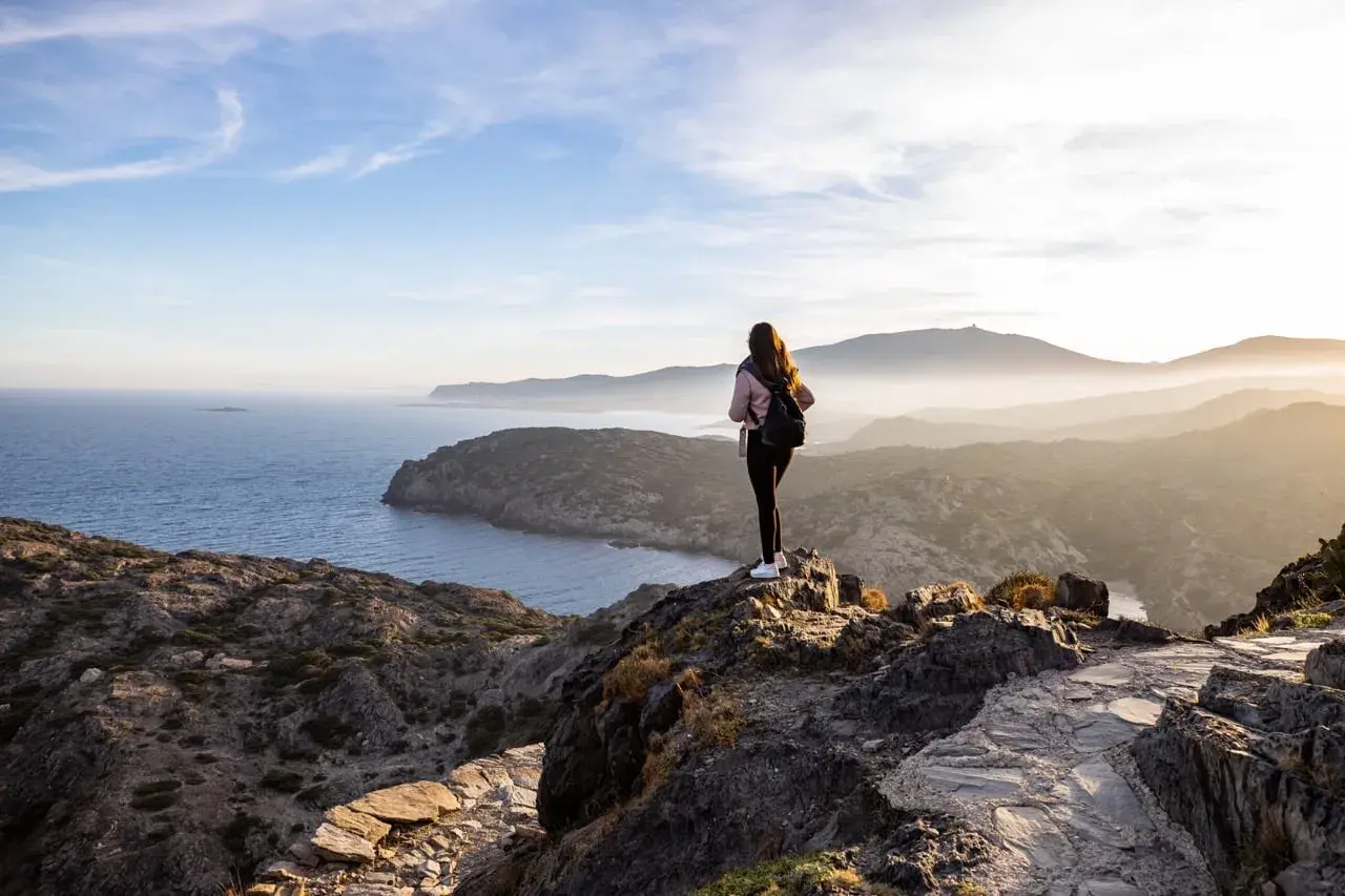 Ensam vandrare njuter av den dramatiska kustlinjen vid Costa Brava. Solen går ner över bergen och havet.