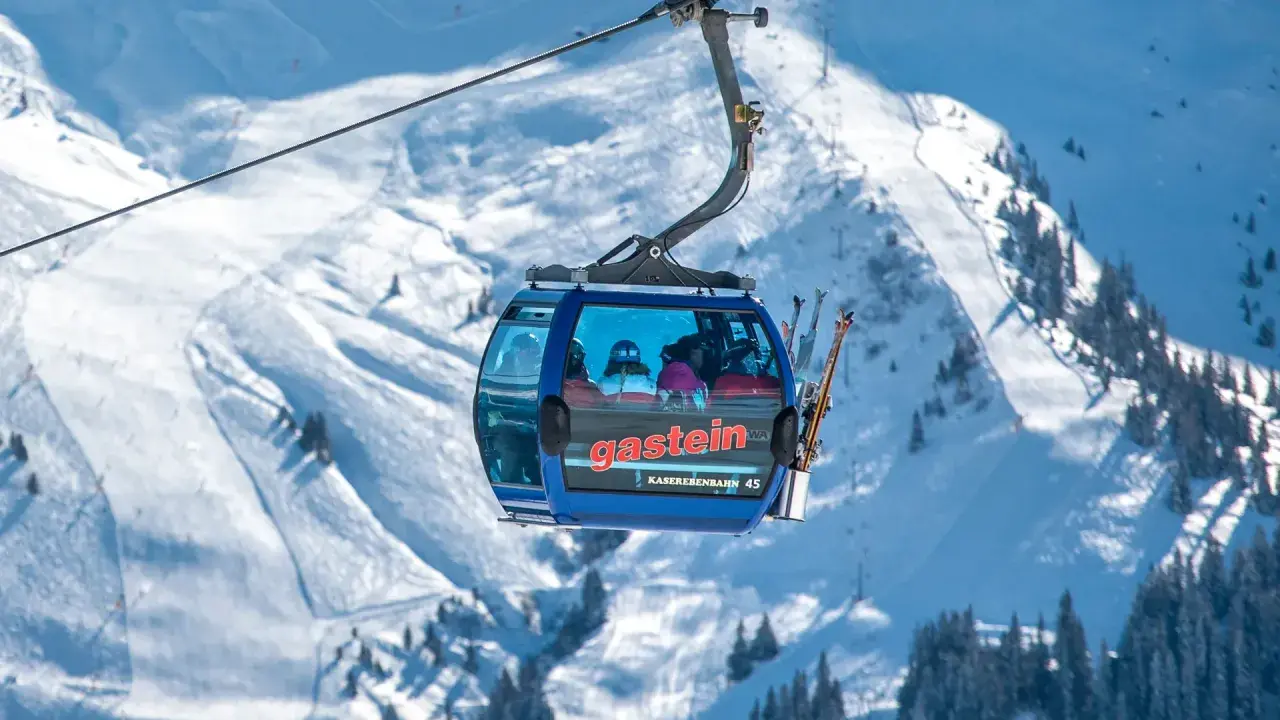 En blå gondol med skidåkare på väg uppför ett snöigt berg. Snart dags för tåg till St. Anton!