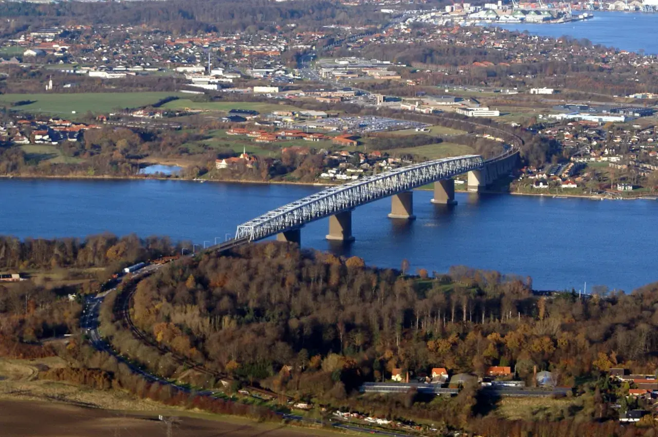 Lilla Bältbron sträcker sig över det blå vattnet, omgiven av höstfärgad skog och en stad i bakgrunden.