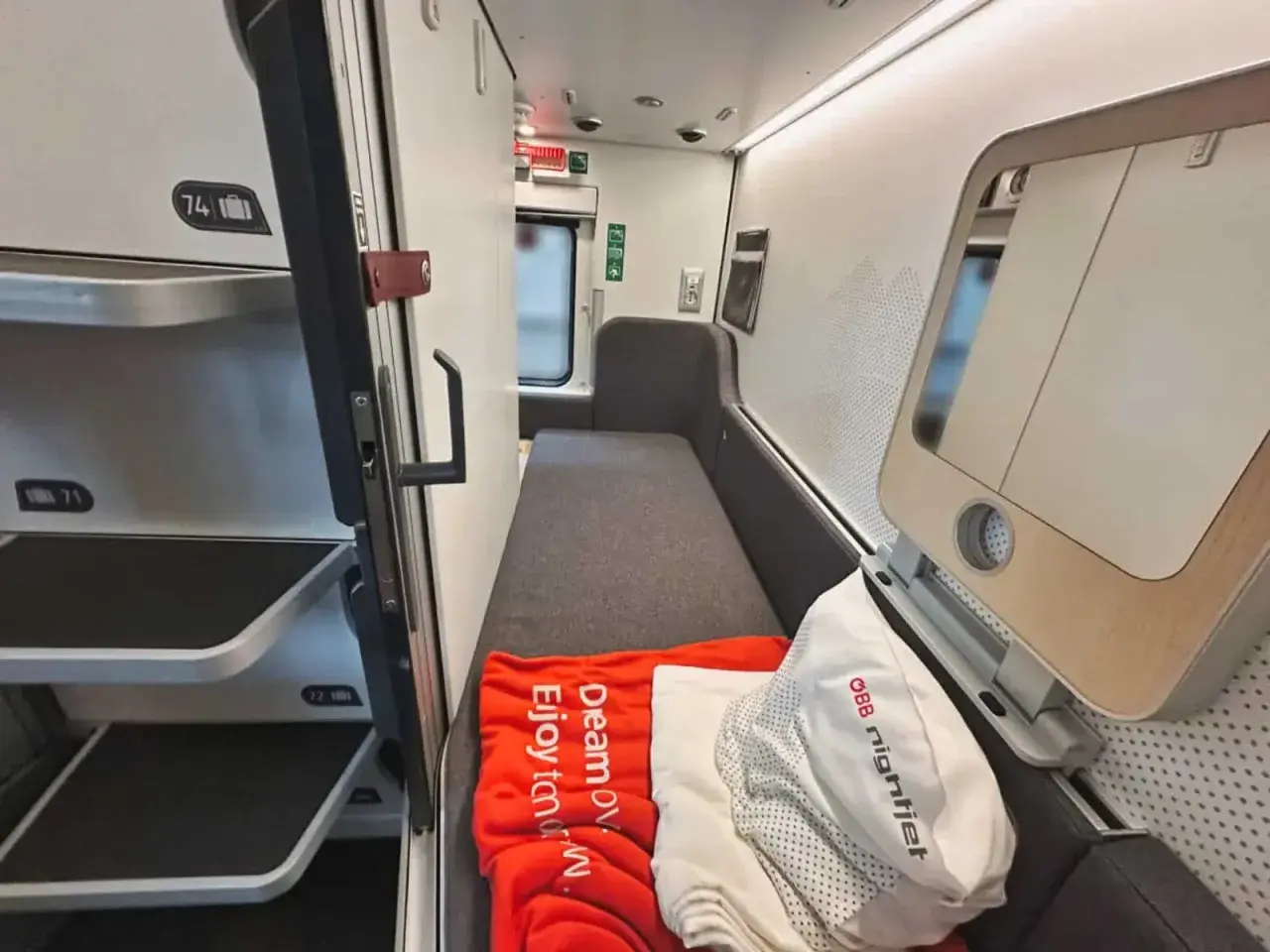 Sovkabin i en Nightjet för Interrail. En orange filt med texten "Dream ov. Enjoy tomorow." ligger på en bädd.