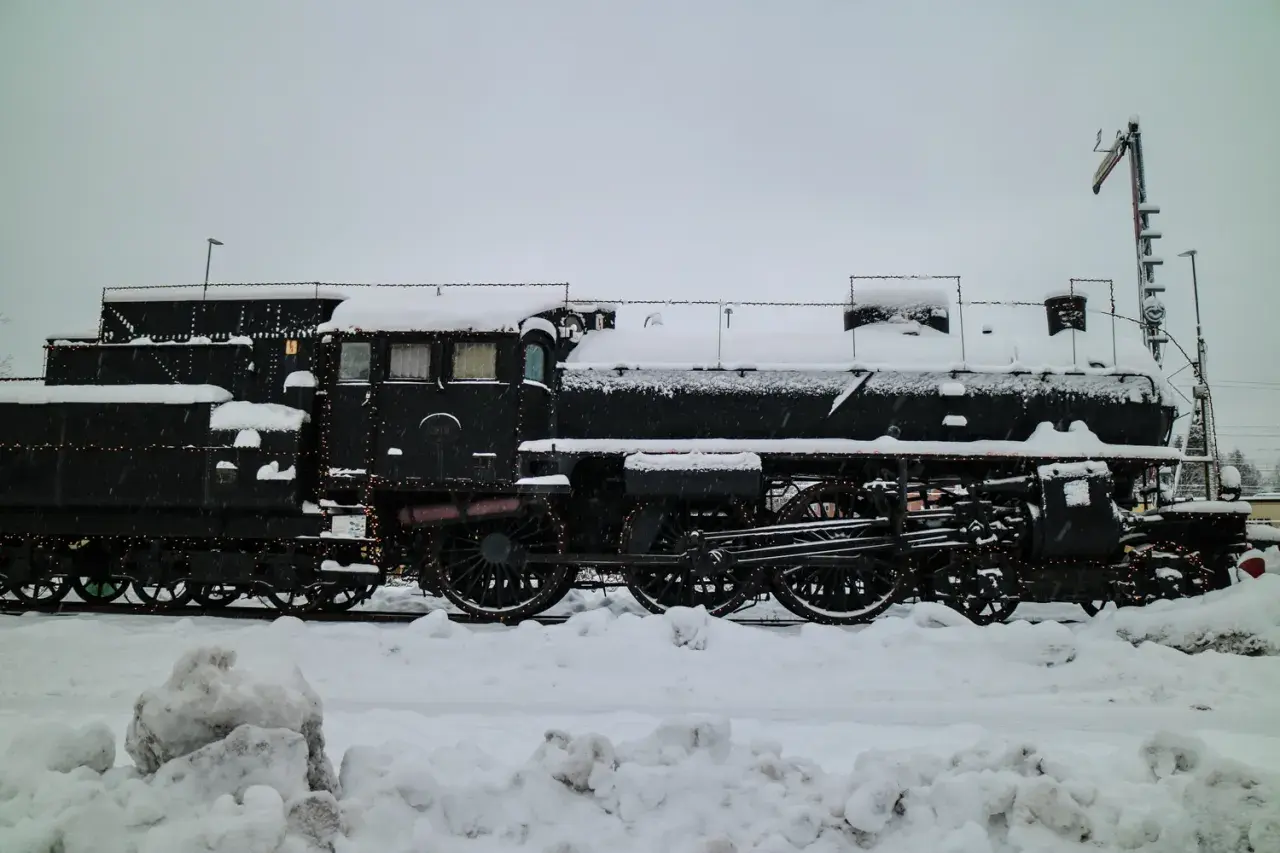 Ett snötäckt ånglok, dekorerat med ljusslingor, står parkerat. Kanske en del av ett biltåg i Tyskland som väntar på våren.