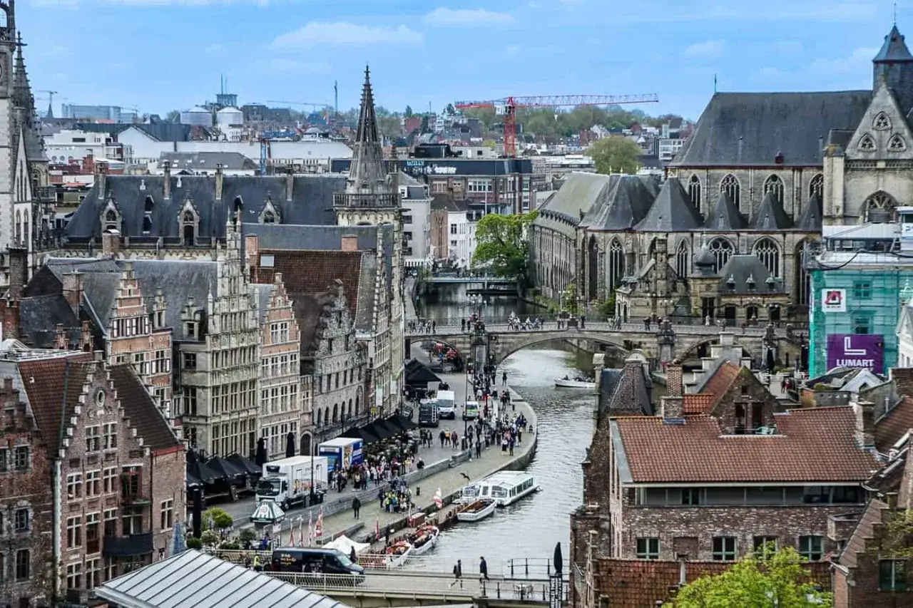 Vacker vy över kanalen i Gent, Belgien, med historiska byggnader och broar. En båt glider fram på vattnet.