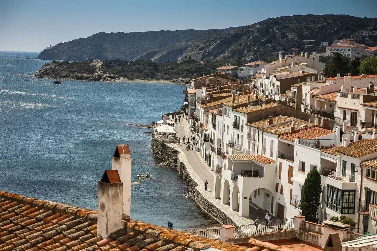 Vitt hus l&auml;ngs kusten vid Costa Brava, med bl&aring;tt hav och gr&ouml;na kullar i bakgrunden.