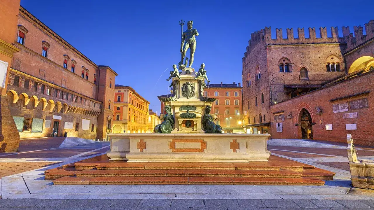 Fontana del Nettuno i dess omgivande byggnader i Bologna, Italien, upplysta i skymningen.