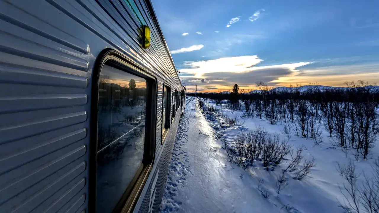 Tåget rullar genom ett snöigt landskap mot Boden, med en vacker solnedgång i horisonten. En resa från Stockholm.