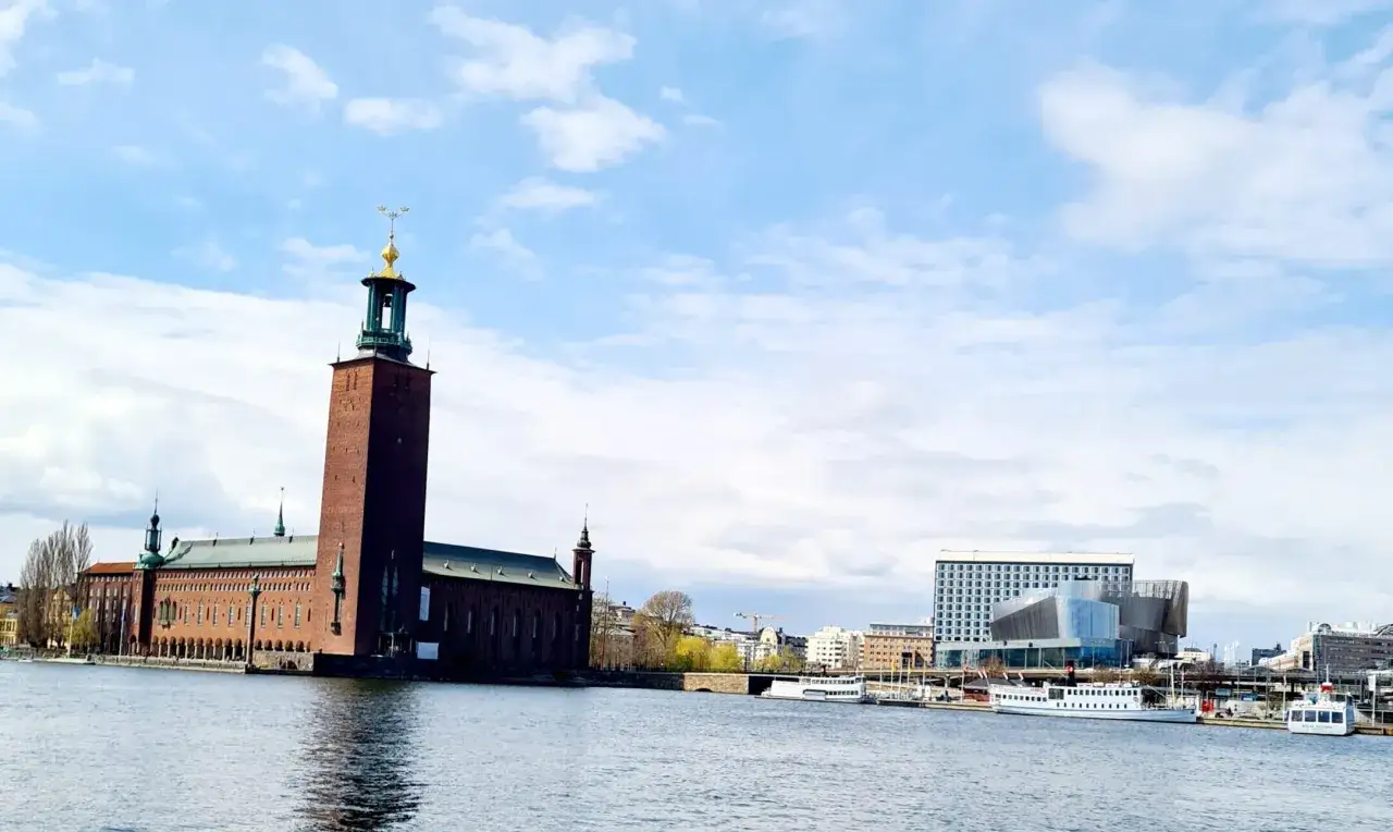 Stadshuset reser sig stolt vid vattnet, en perfekt vy för en hemester i Stockholm. Båtar ligger förtöjda i hamnen.
