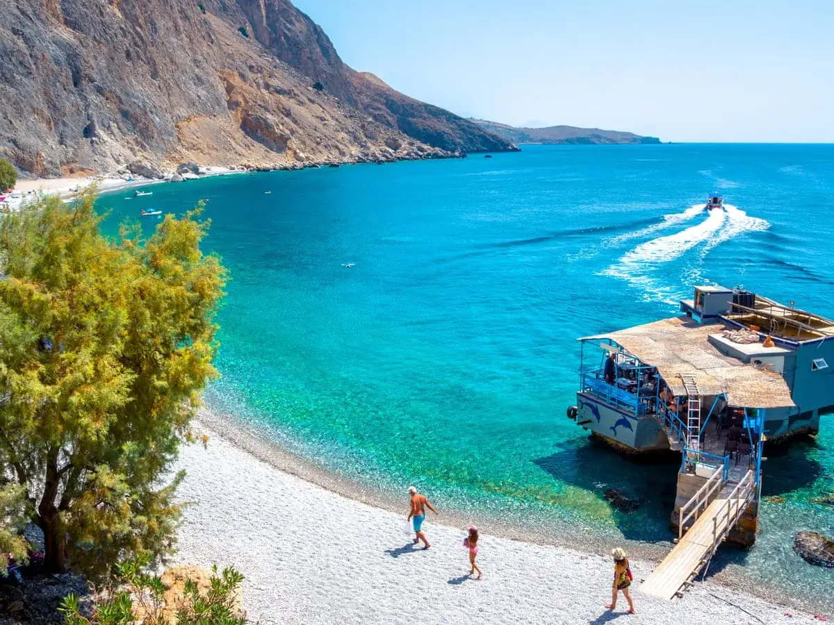 En familj njuter av sin solsemester i Europa vid en turkos strand med en flytande restaurang.