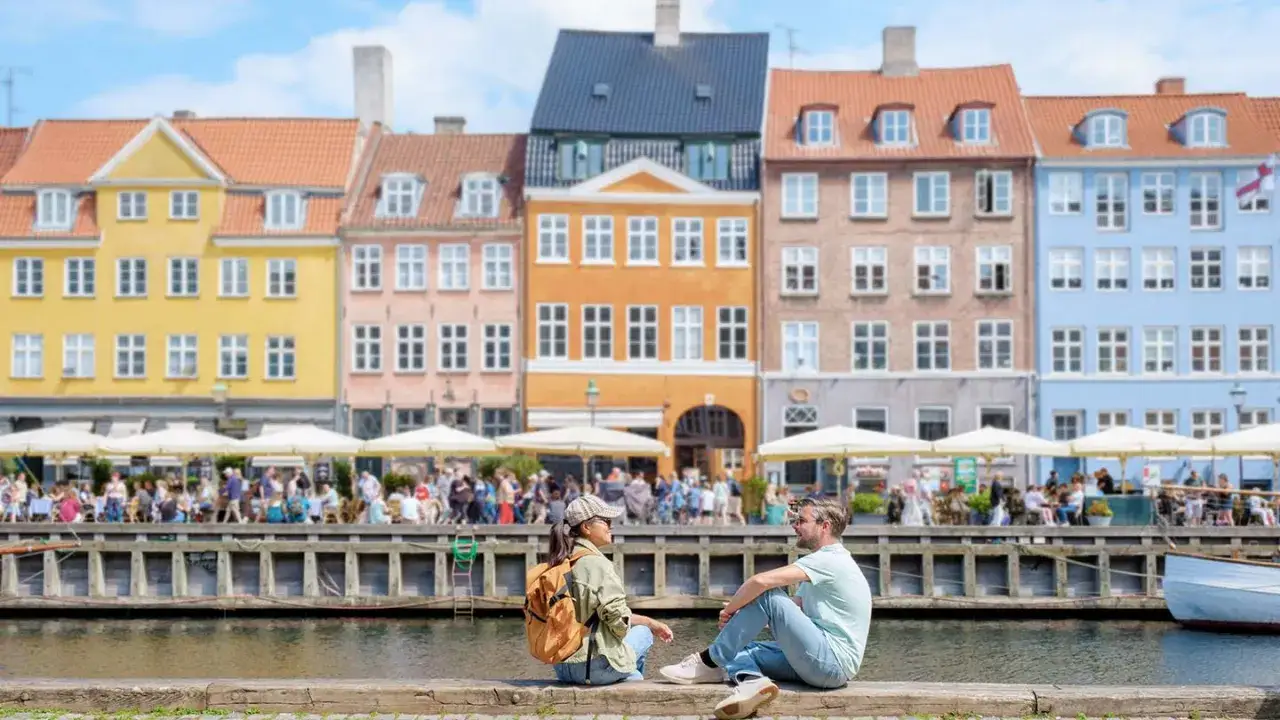 Ett par njuter av utsikten över Nyhavn i Köpenhamn, perfekt för weekendresor till Danmark. Färgglada hus och folkliv vid vattnet.