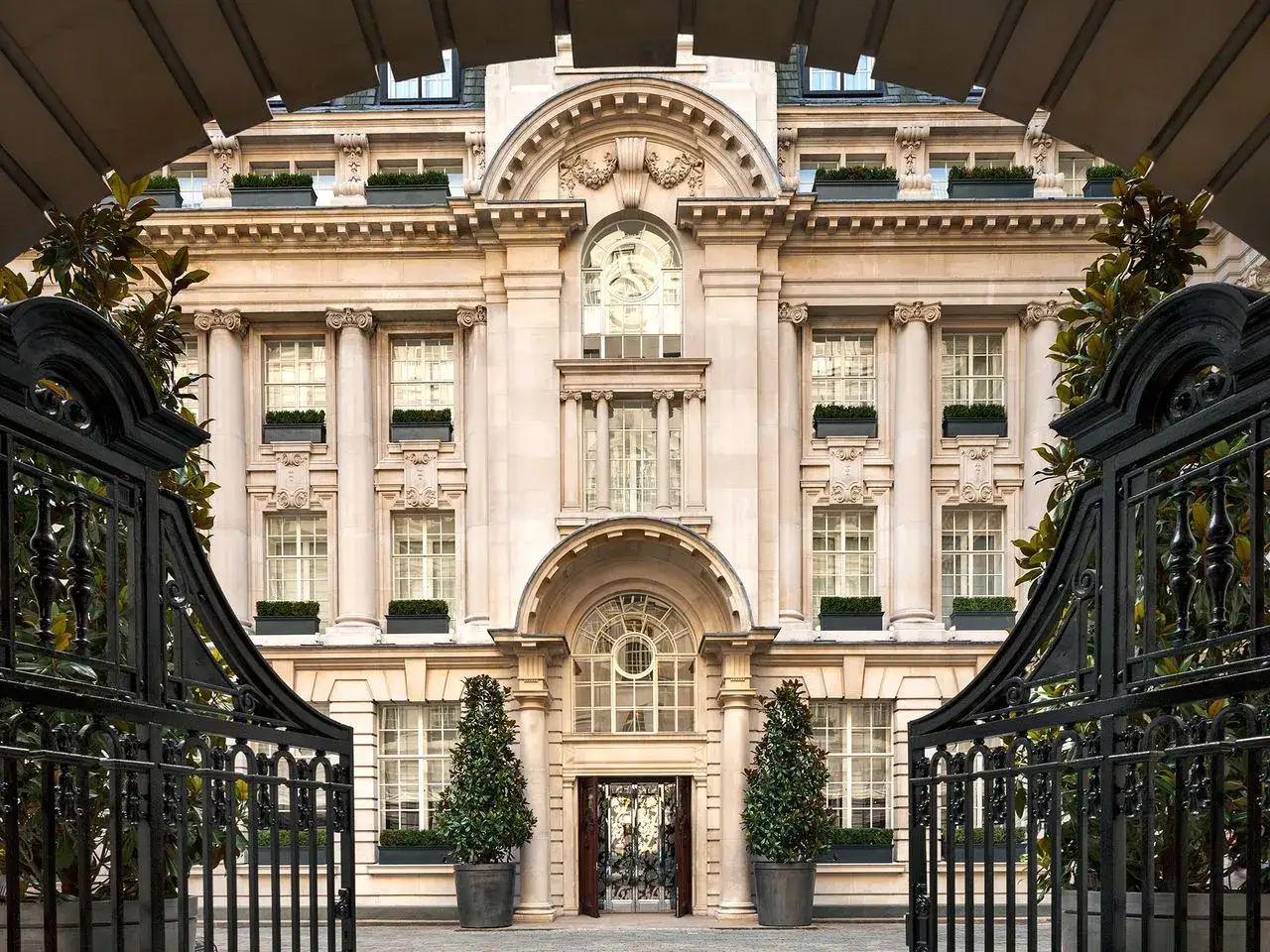 Imponerande fasad med klassiska pelare och fönster, en glimt av Londons lyxigaste hotell bakom en elegant smidesjärnsgrind.