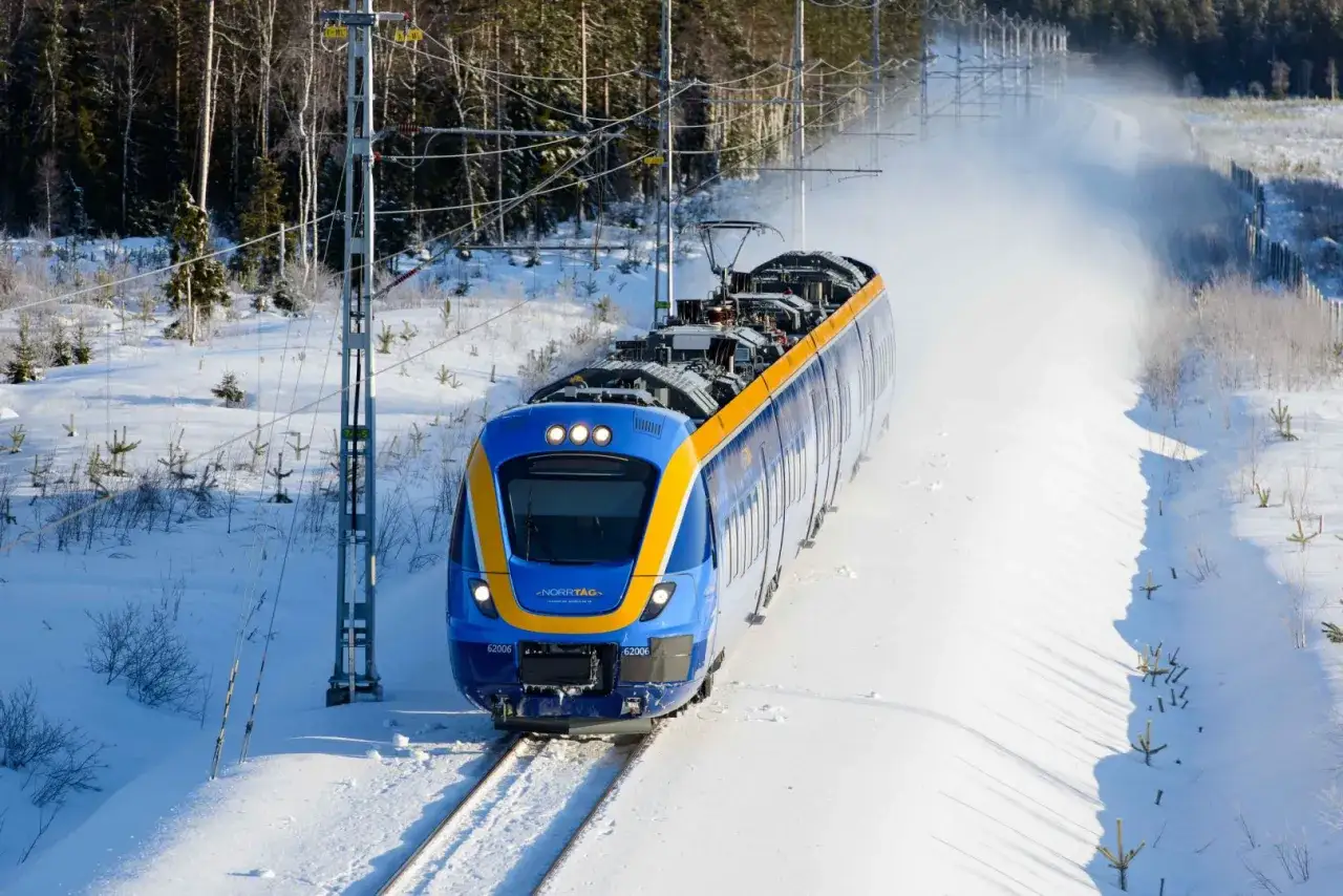 Bl&aring;tt och gult t&aring;g till Sundsvall k&ouml;r genom ett sn&ouml;igt landskap med skog i bakgrunden.