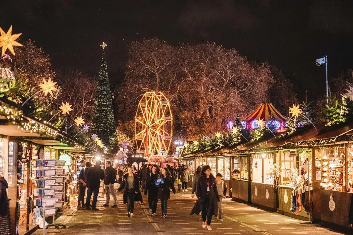 En livlig julmarknad i Europa med ett stort julgransprytt träd, ett pariserhjul och många stånd.