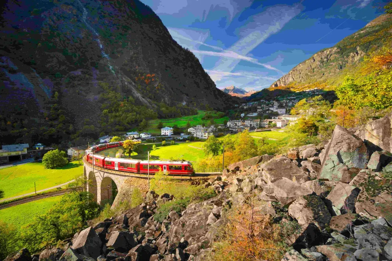 Rött tåg på en stenbro i en dal med gröna ängar och ett litet samhälle. En resa från München till Innsbruck kan se ut så här.