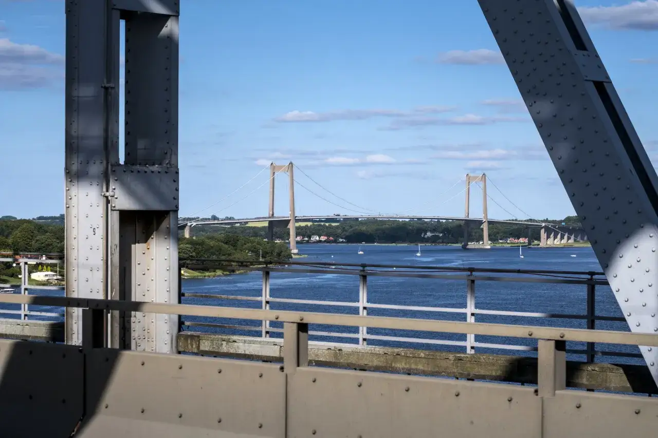 Lilla Bältbron sträcker sig över det blå vattnet, med segelbåtar som glider fram. En solig dag med moln på himlen.