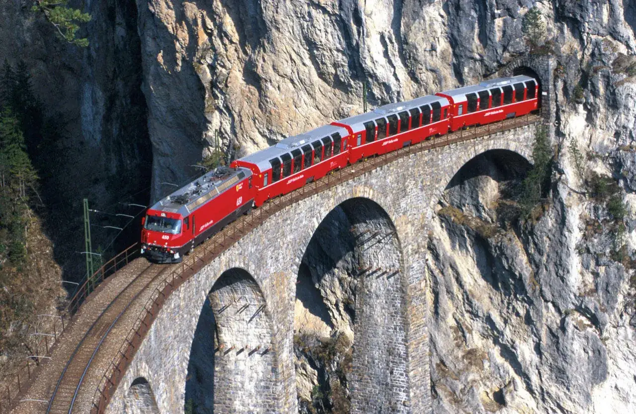 Rött tåg på en stenbro över en ravin, en fantastisk vy för en interrail-resa genom Alperna.