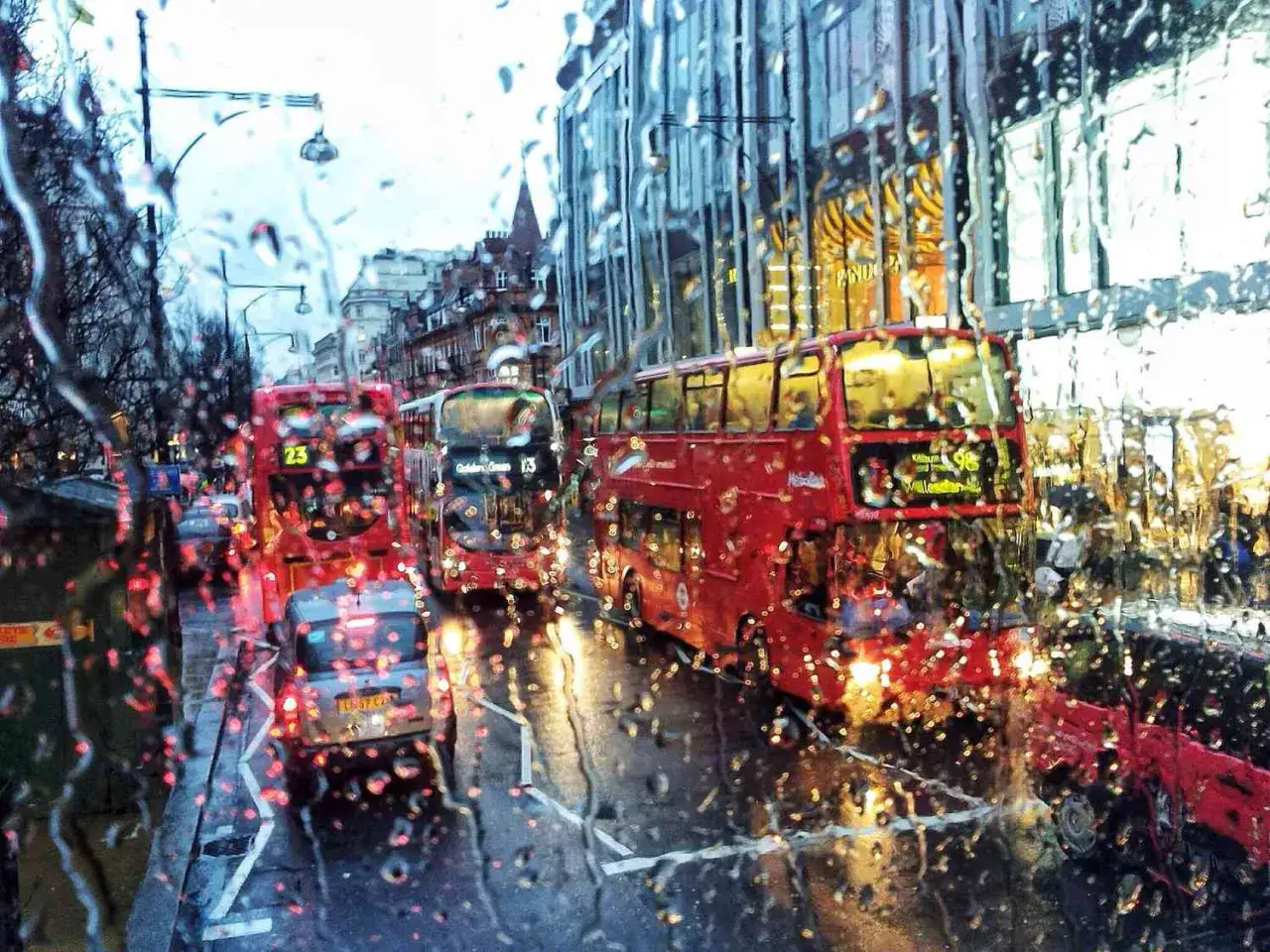 Regniga gator i London med röda dubbeldäckare. Typiskt klimat London, med droppar på fönstret som skapar en drömsk atmosfär.