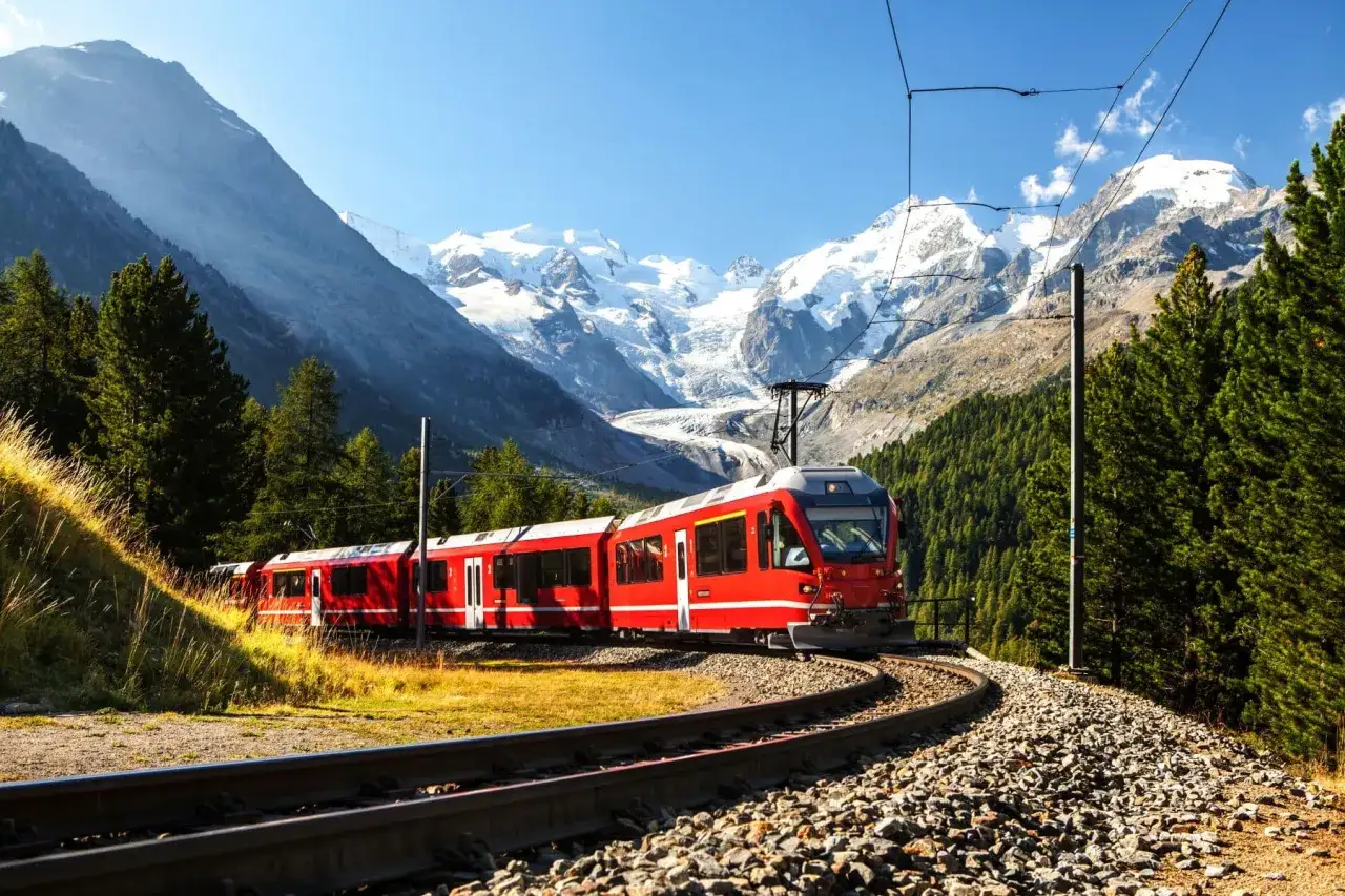 Rött tåg i bergig terräng med snöklädda toppar. En drömresa med interrail pris som väntar.
