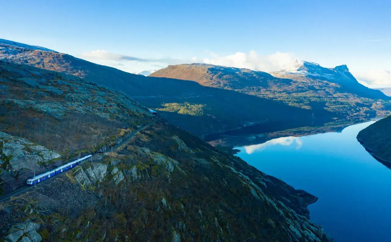 Blått tåg slingrar sig längs bergssluttning vid en spegelblank fjord. En resa mellan Kiruna och Narvik genom storslagen natur.