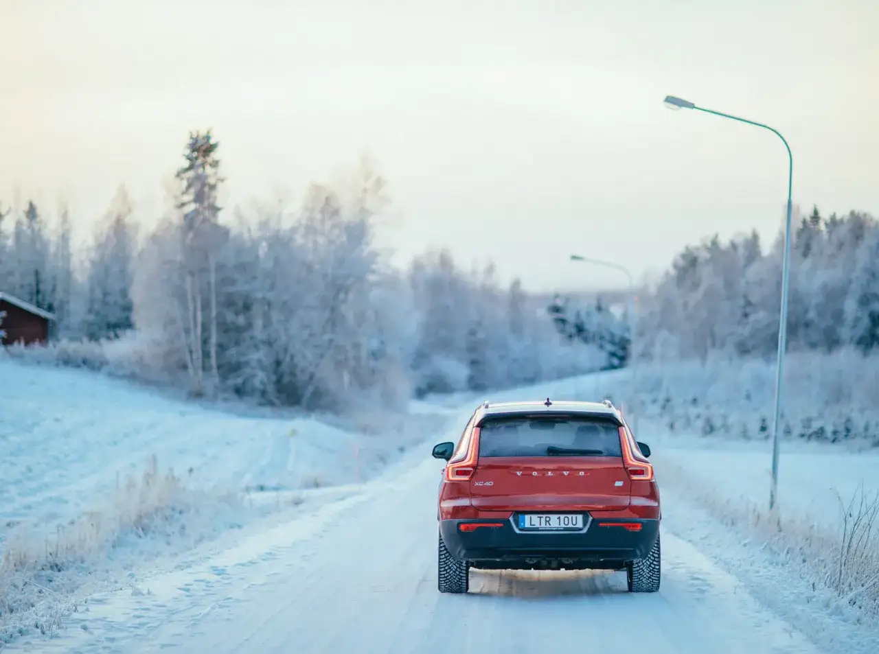 Röd Volvo XC40 kör på en snöig väg, redo för resan från Stockholm till Oslo. Vinterlandskap med frostiga träd.
